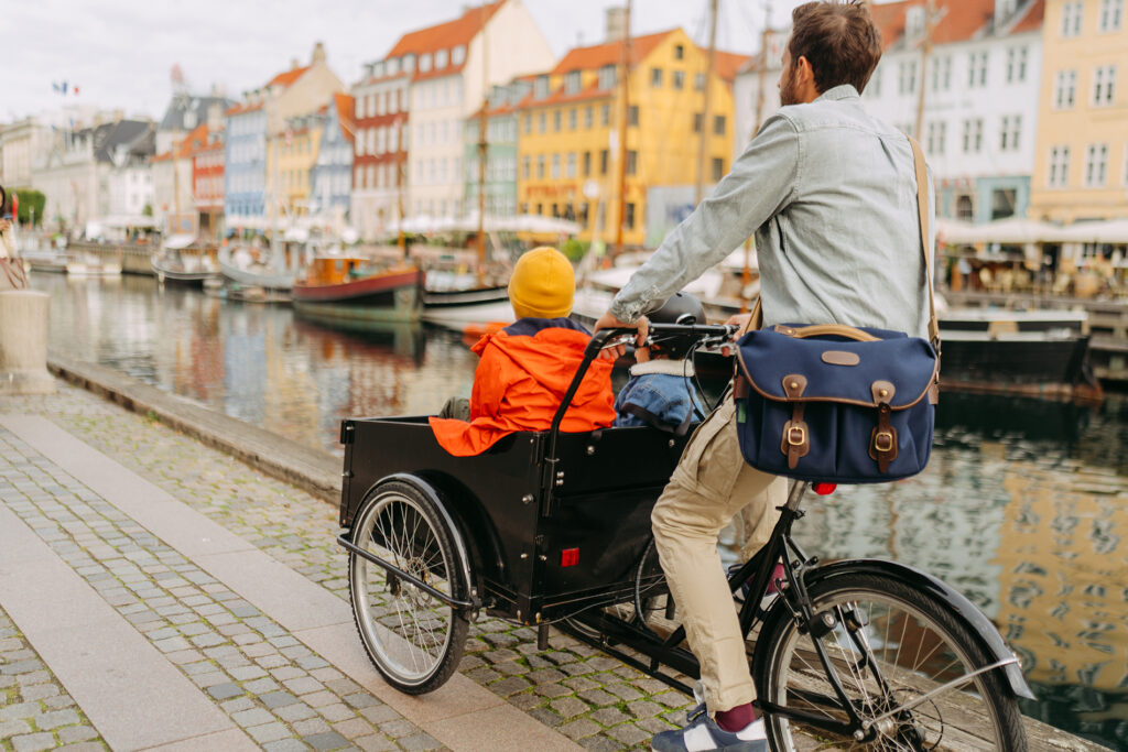 Photo of two boys riding in a cargo bike with their father in downtown of Copenhagen
